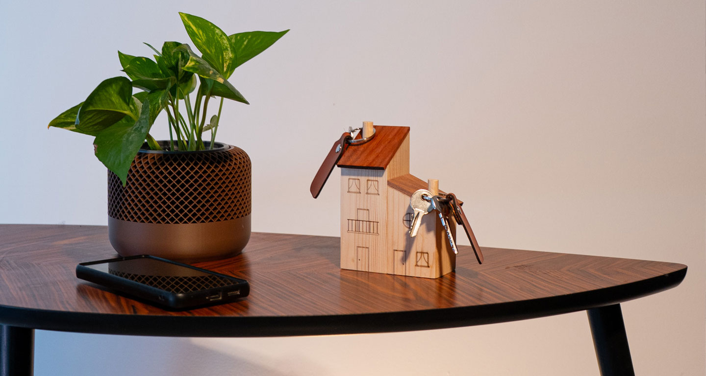 Fotografía de estudio del conjunto de peana o porta-llaveros con diseño de casitas de madera y su juego de llaveros de cuero grabados y cortados a láser